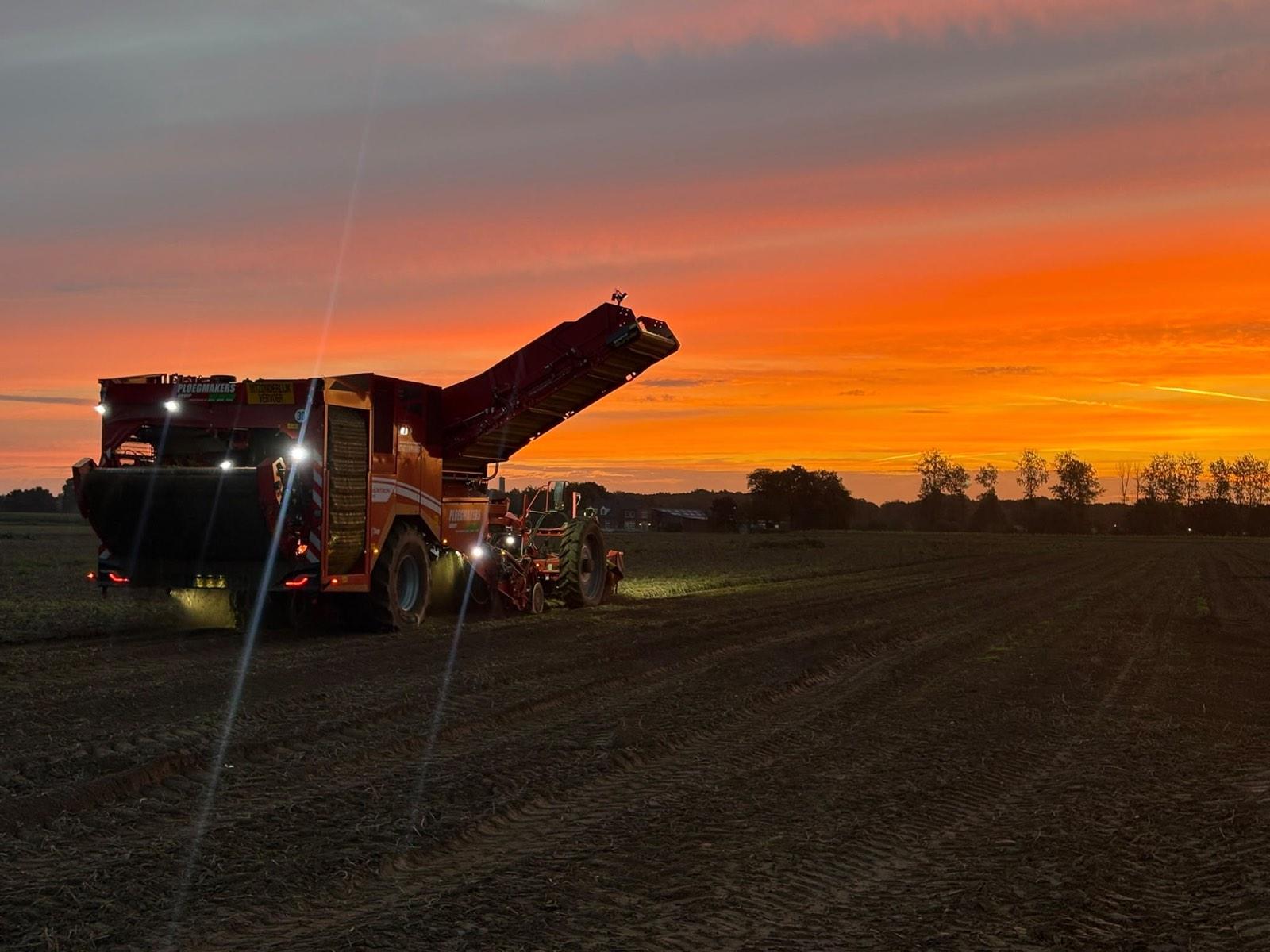 Rode aardappelrooier op het land bij een oranje zonsondergang