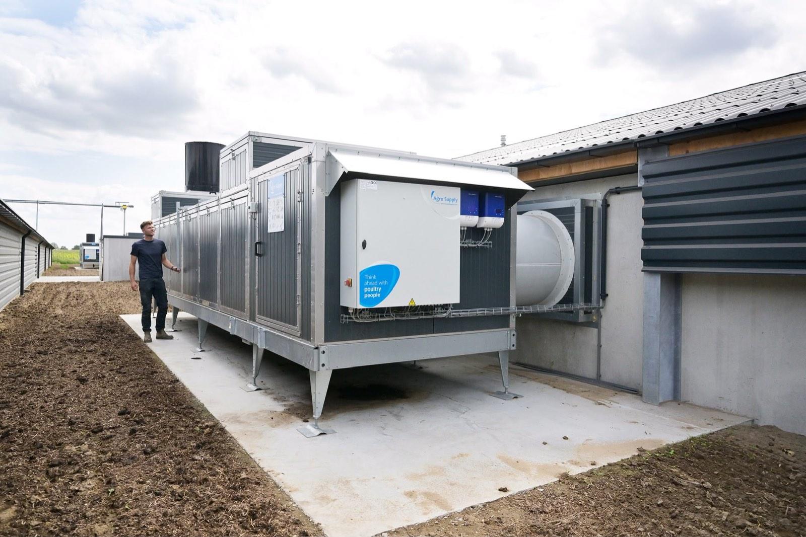 Een man naast de grote warmtewisselaar die de verse lucht voor de stal voorverwarmt